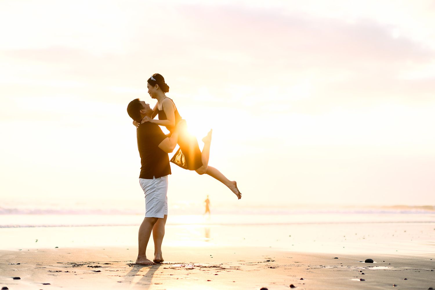 Man lifting woman in the air on a sunny beach with golden sunset light.