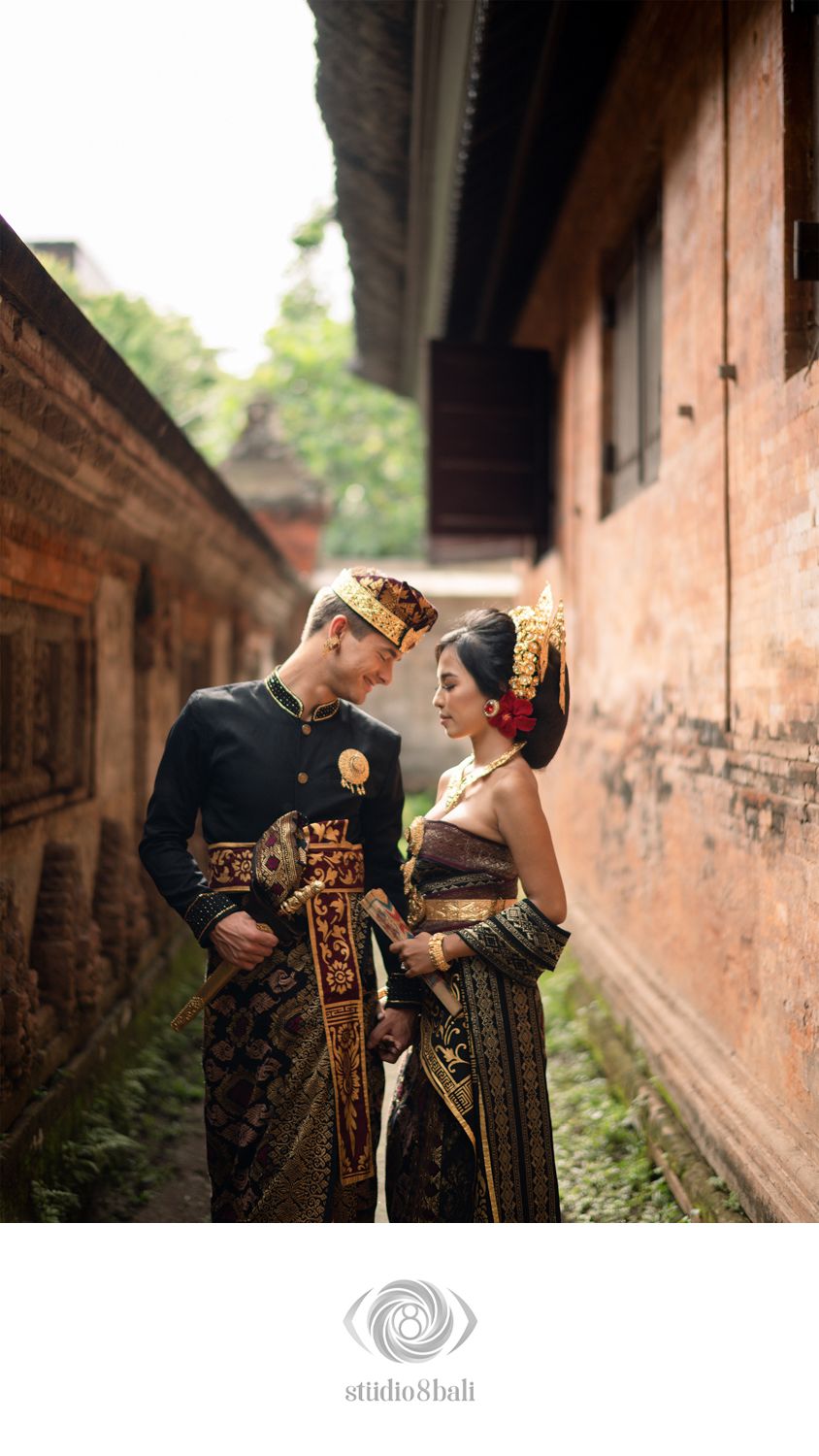 Couple in traditional Balinese wedding attire standing in an ornate temple corridor in Bali, Indonesia.