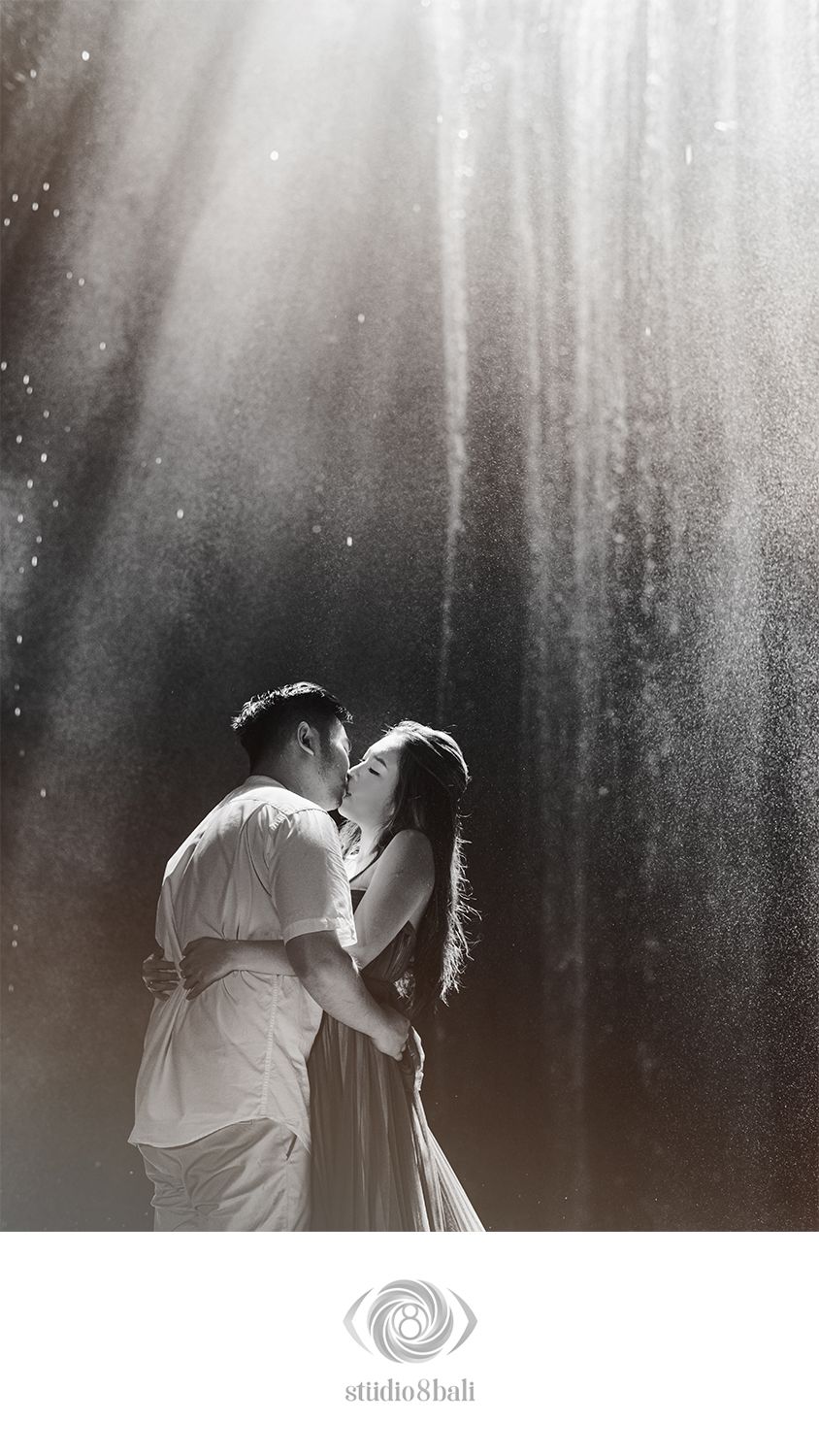 Romantic couple kissing in rain with dramatic light rays, black and white pre-wedding photo by Studio 8 Bali.