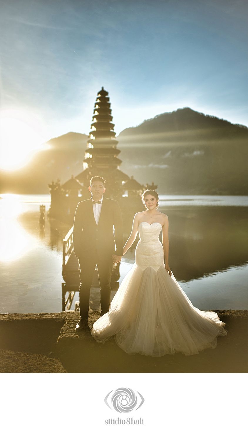 Couple in wedding attire posing at Pura Ulun Danu Bratan temple in Bali at golden hour.