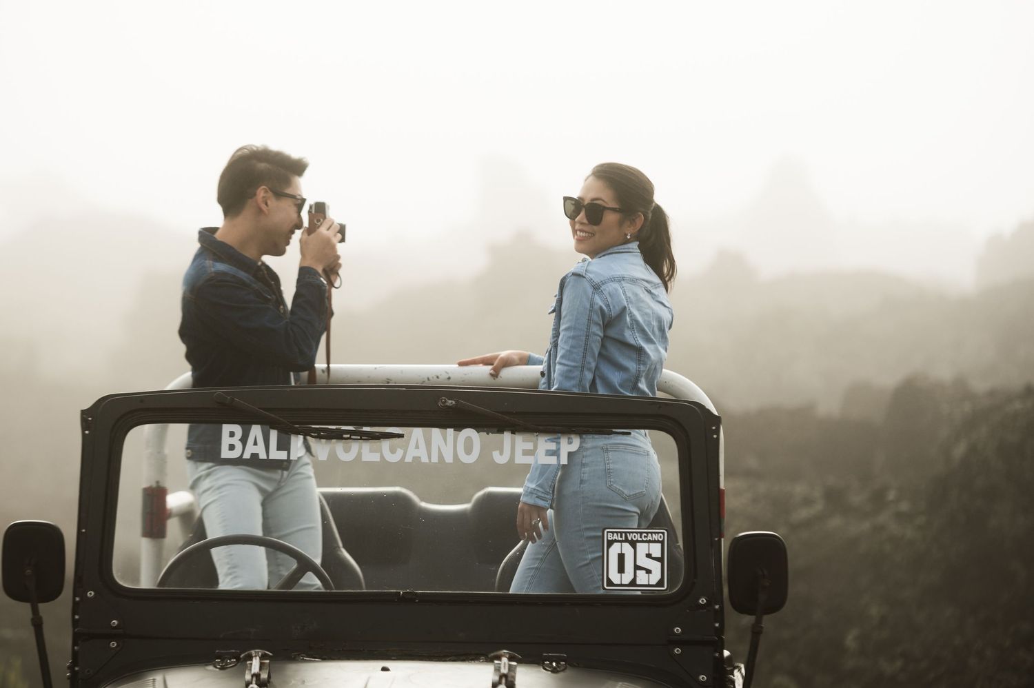 Couple riding in a Bali Volcano Jeep tour through misty volcanic landscape, man photographing scenery.