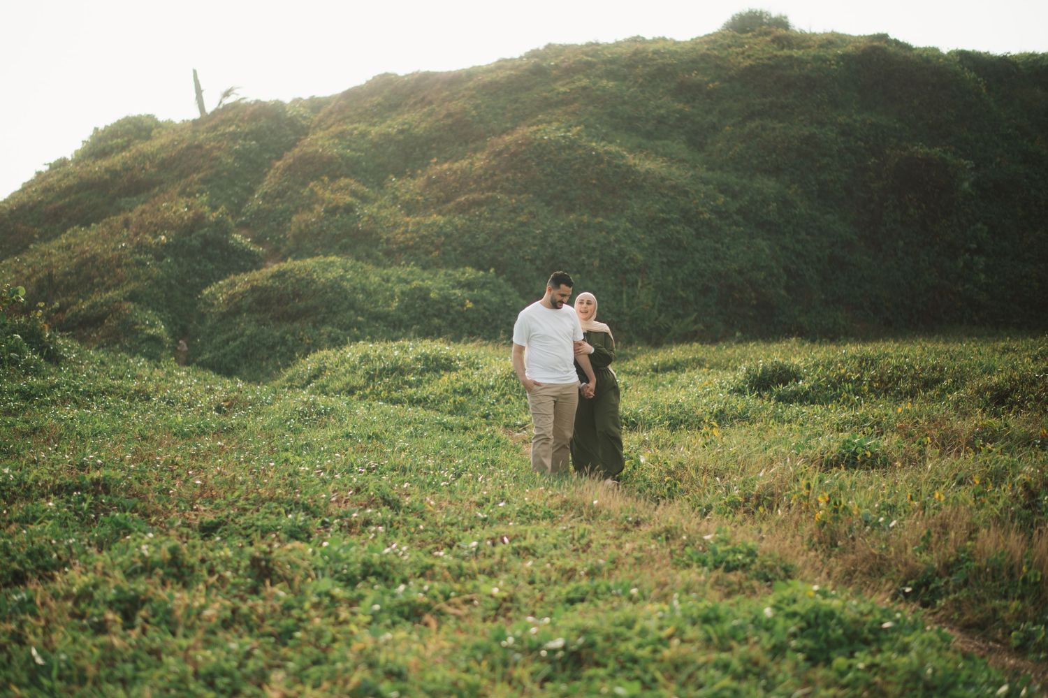 Couple embracing on a lush green hillside at golden hour in a romantic outdoor setting.
