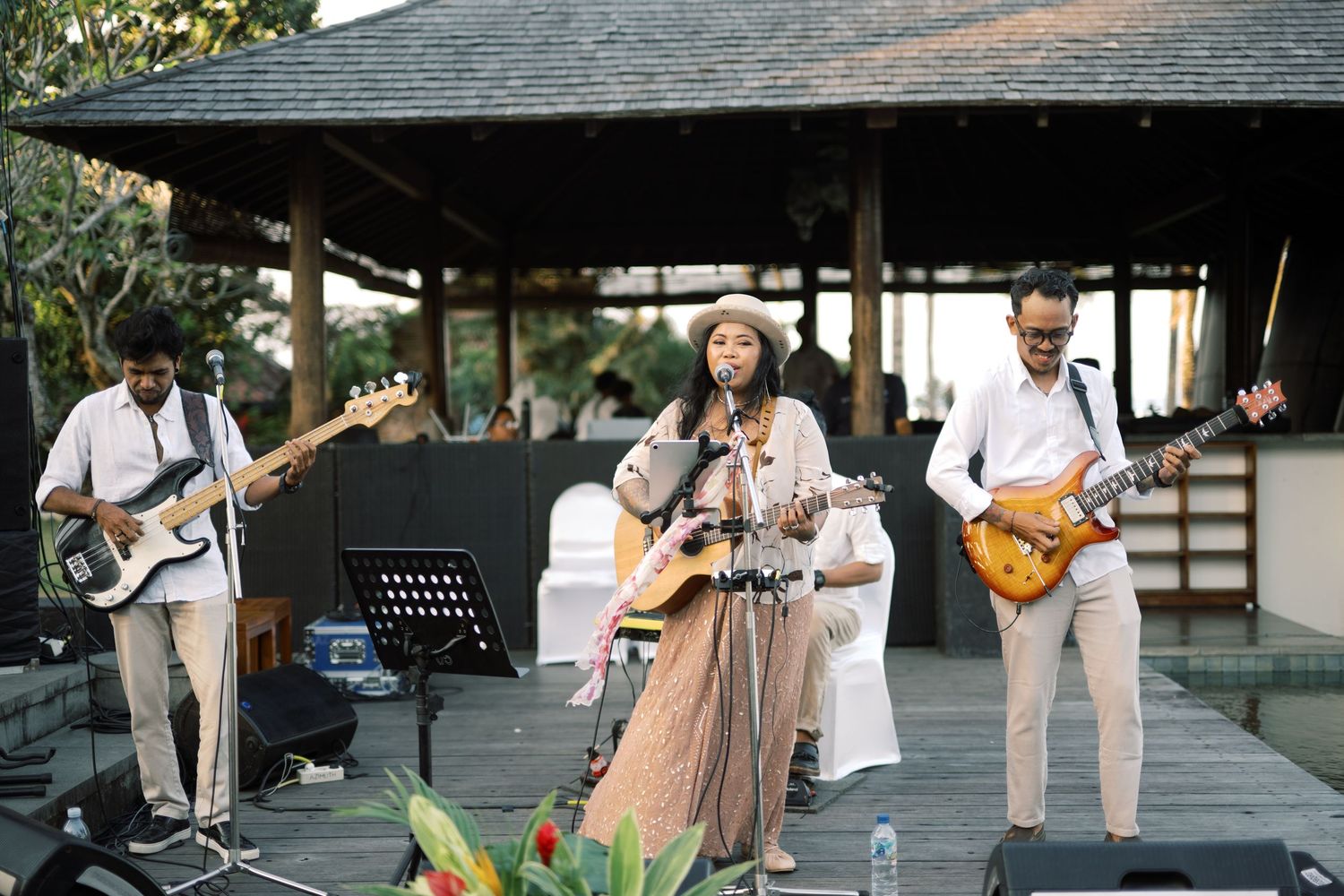 Live band performing outdoors with female vocalist and two guitarists on a wooden stage at an elegant venue.