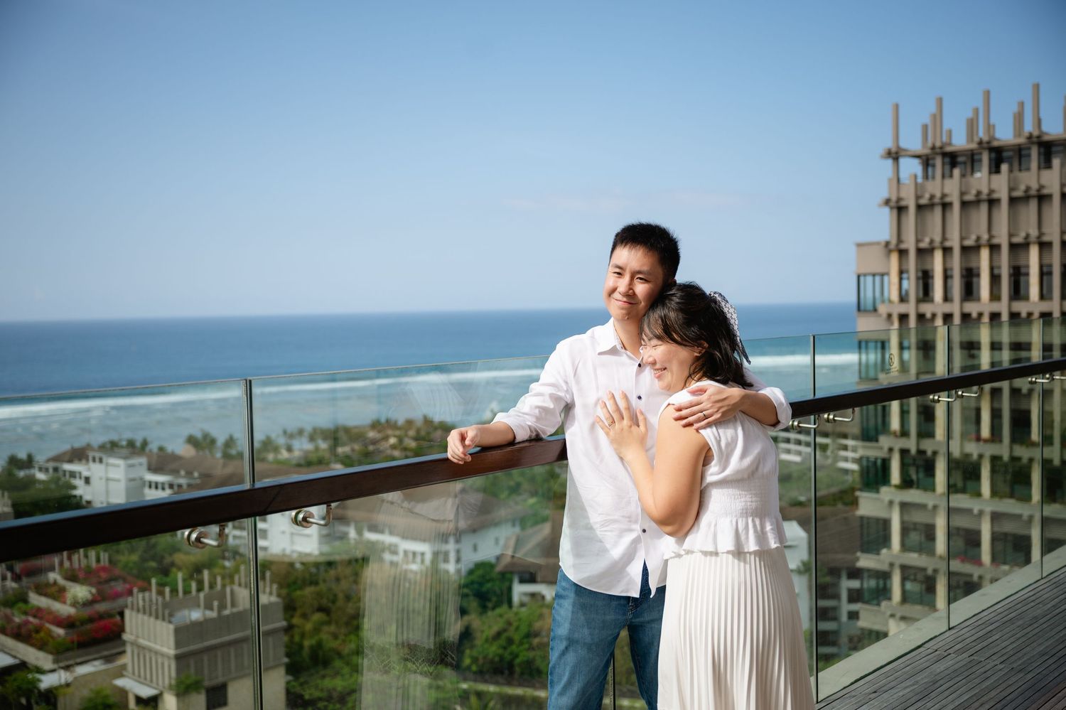 Couple embracing on a balcony with ocean view and blue sky, romantic outdoor moment at a seaside resort.