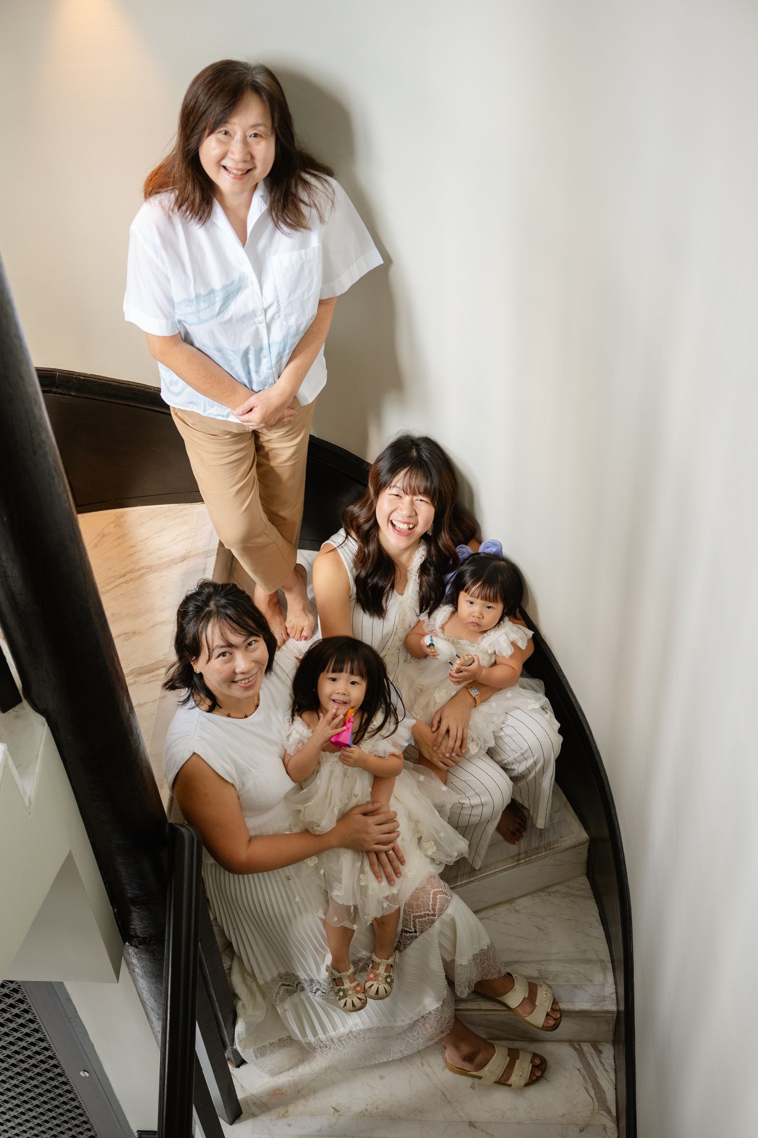 Family of five posing on curved staircase, two adults and three children smiling, wearing white and neutral tones.