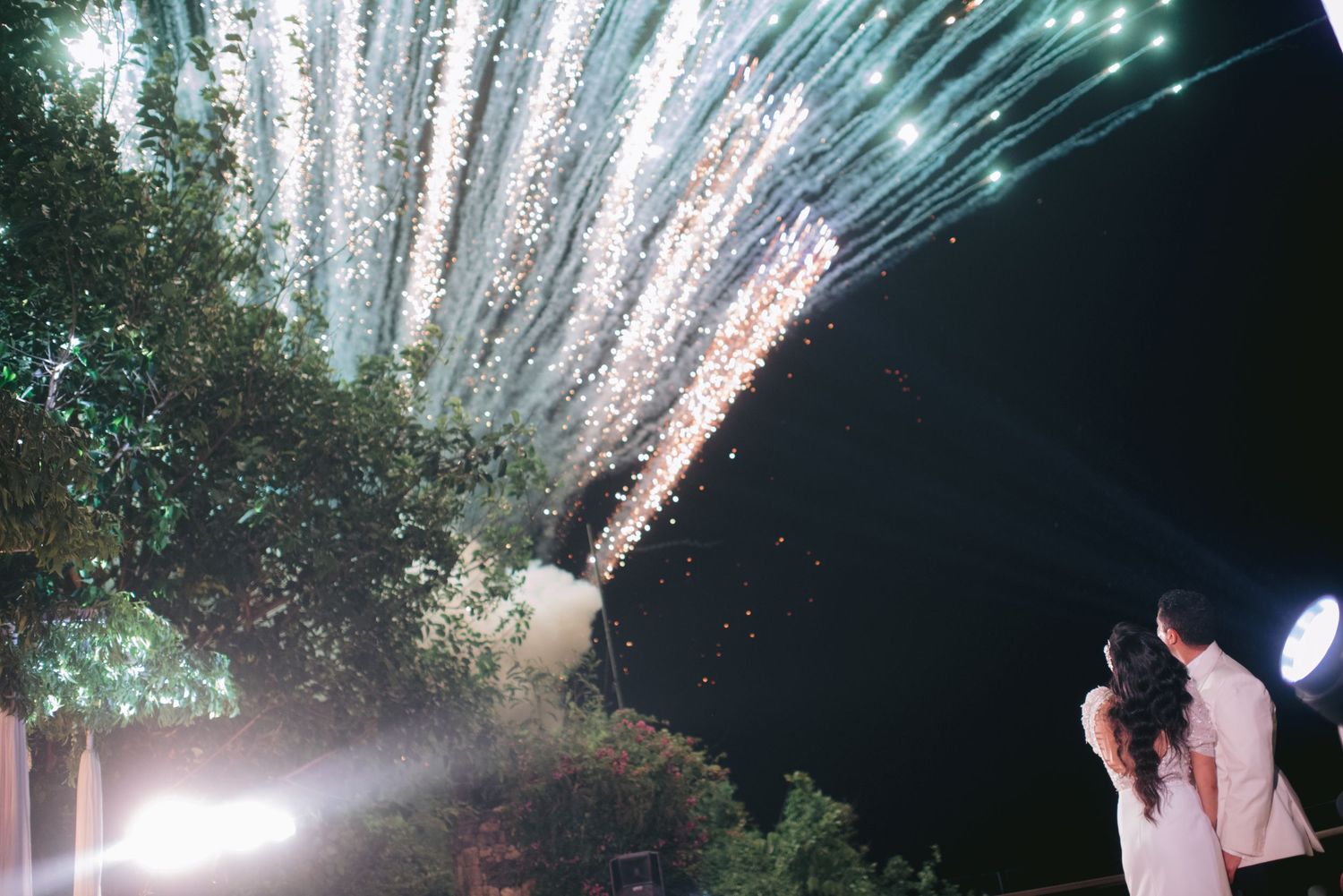 Couple watching stunning wedding fireworks display lighting up the night sky with sparkling cascades.