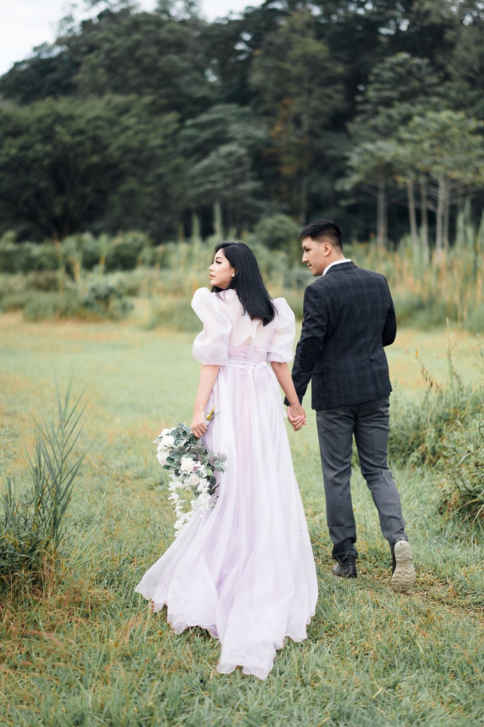 Couple in wedding attire holding hands in a lush green field, bride in pink gown holding bouquet.
