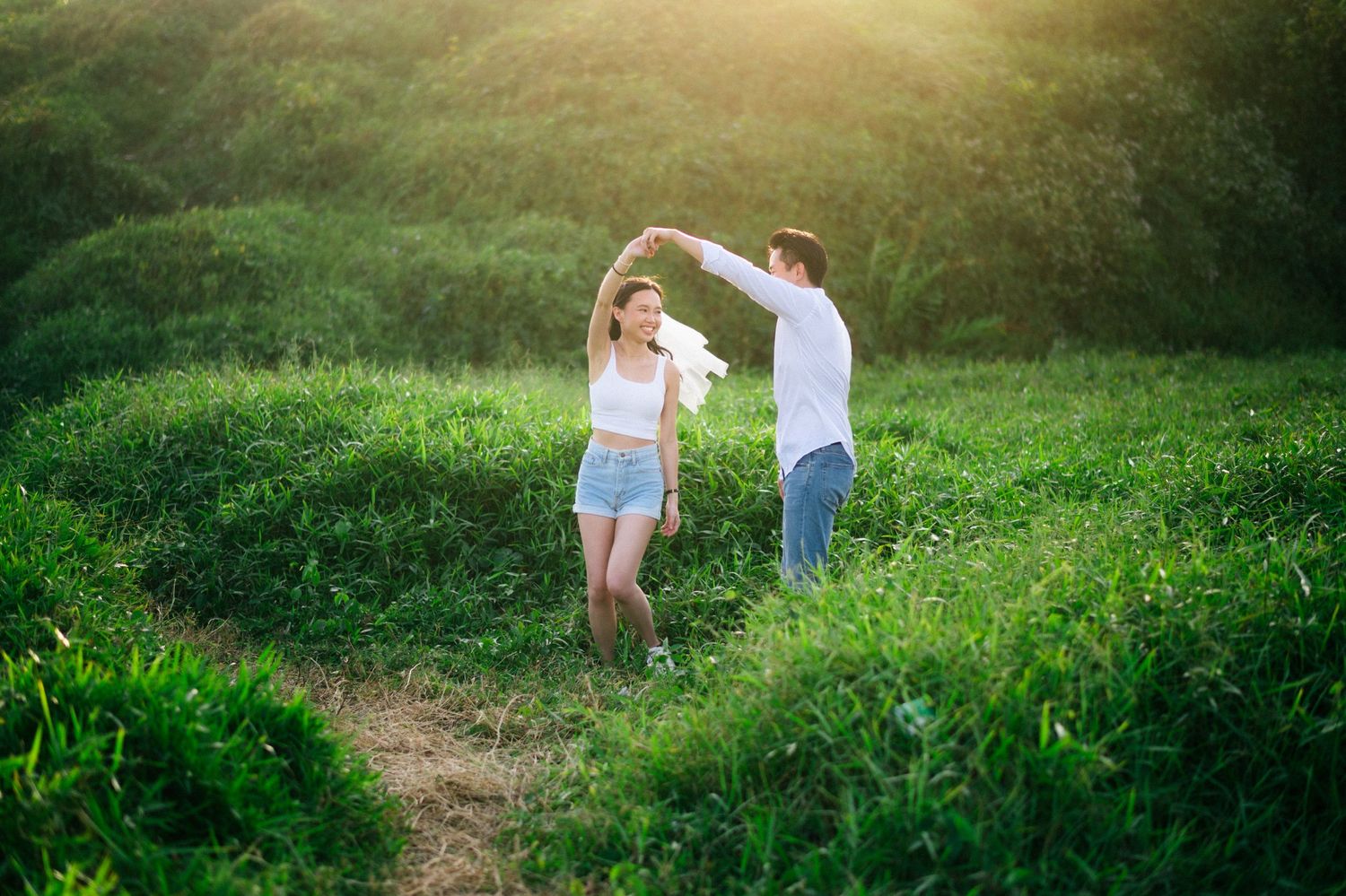 A couple dances joyfully in a lush green field, bathed in warm golden sunlight.