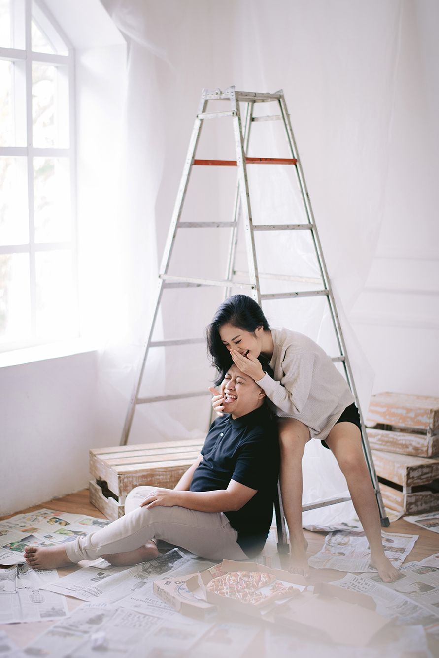 Couple relaxing on floor near ladder in bright white room during home renovation project.