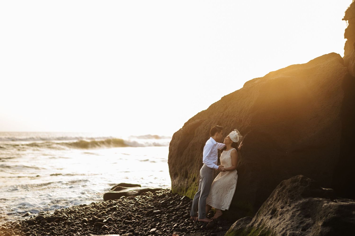 Couple embracing near rocky cliffs at golden sunset on a scenic ocean beach.