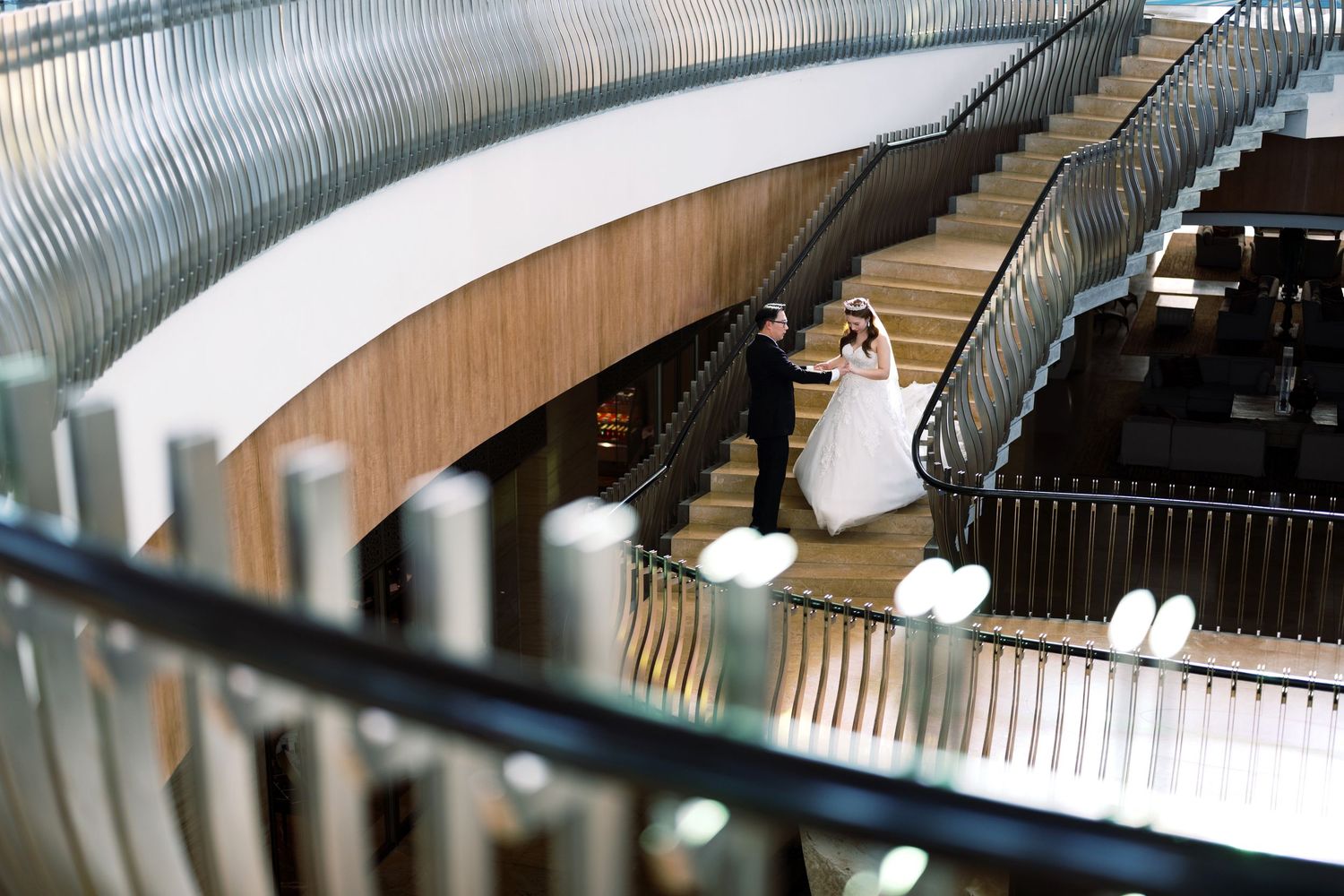 Bride and groom share a romantic moment on a grand staircase in an elegant modern venue.