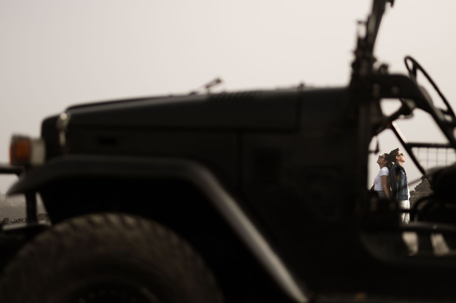 Military jeep in foreground with a person visible in the background on a hazy day.
