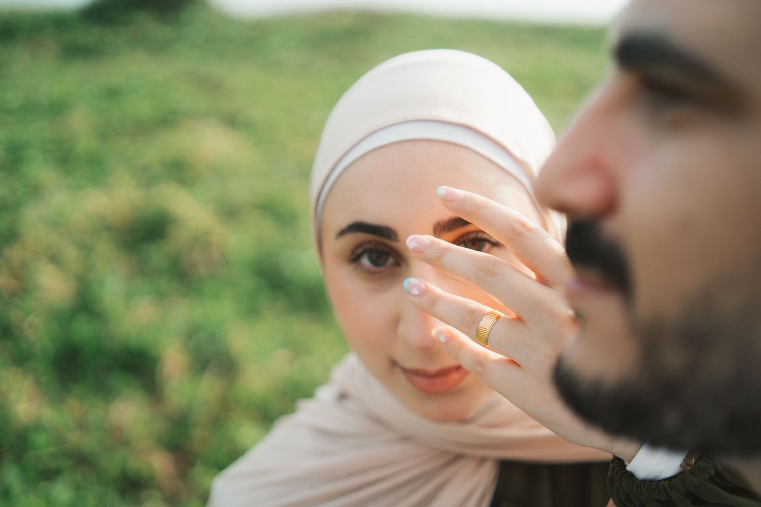 Muslim couple in nature, woman in hijab with engagement ring visible, romantic outdoor portrait.