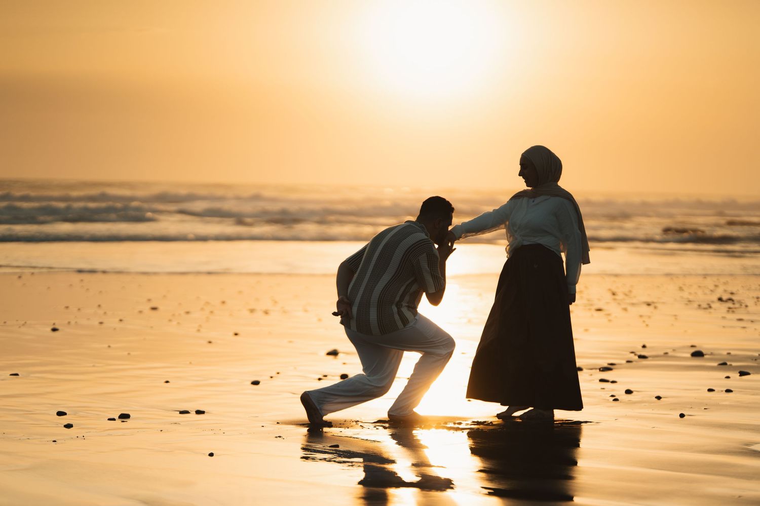 Silhouettes of two people practicing martial arts on a beach at golden sunset with ocean waves in the background.