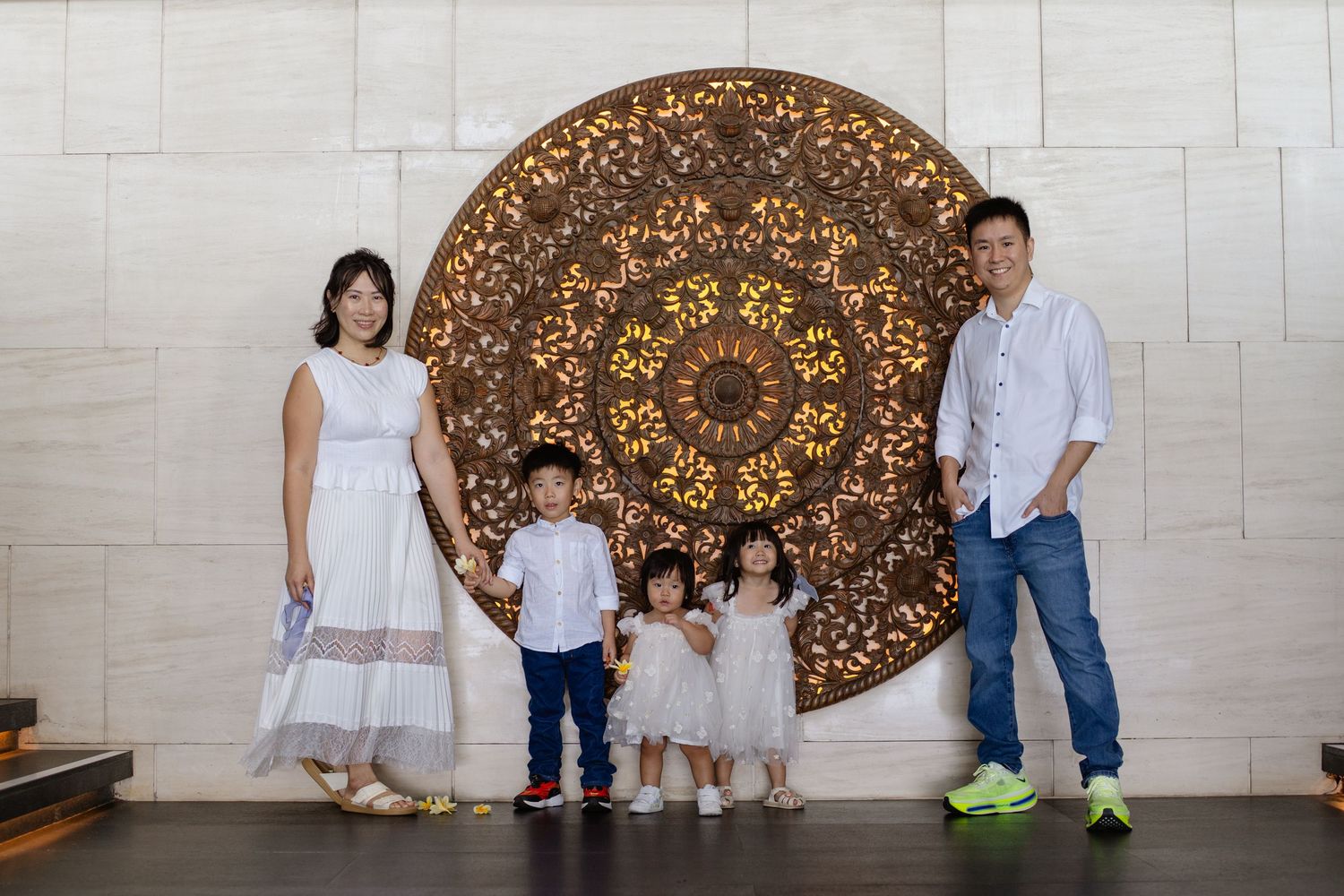 Asian family of five posing in front of ornate wooden mandala wall art in elegant interior space.