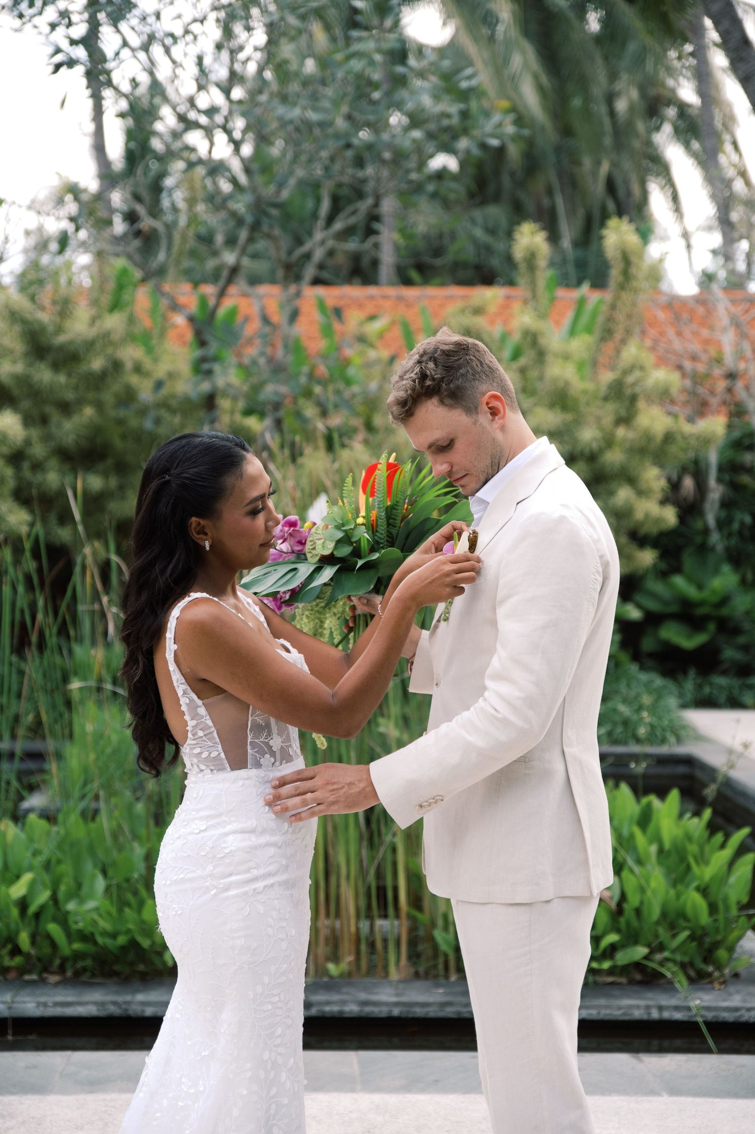 Bride and groom share first look moment with vibrant tropical bouquet in lush garden setting.