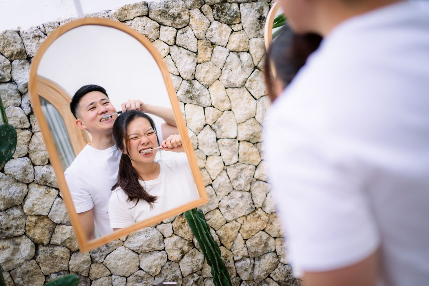 Couple smiling in arched mirror reflection against stone wall, man styling womans hair outdoors.