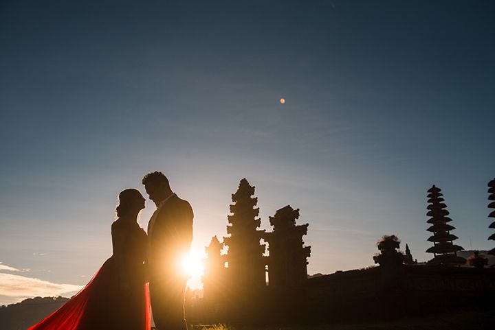 Silhouette of a couple in romantic pose at sunset with Balinese temple architecture and glowing sky backdrop.