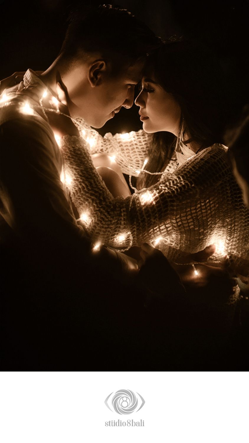 Romantic couple wrapped in glowing string lights sharing an intimate moment in a dark, cozy setting.