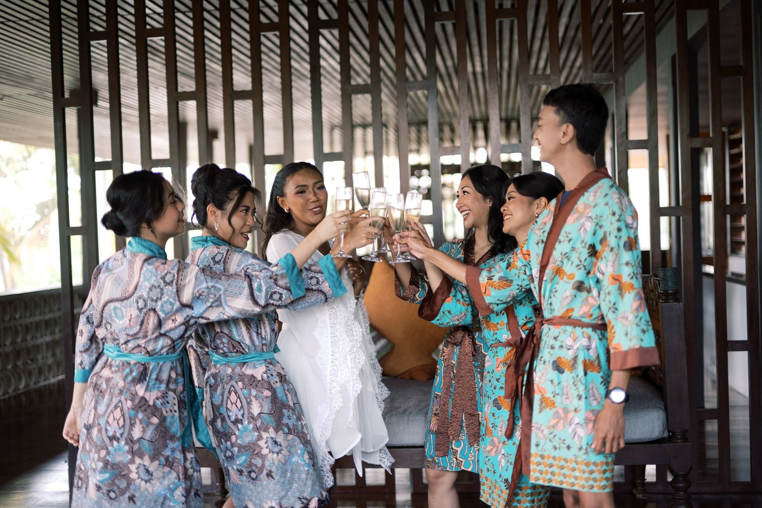 Bridesmaids in colorful robes toasting with champagne glasses during a wedding celebration.