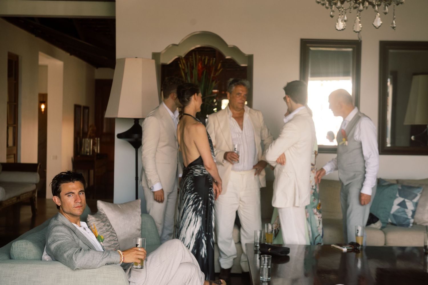 Wedding guests in formal attire mingle inside an elegant villa during a tropical destination wedding reception.