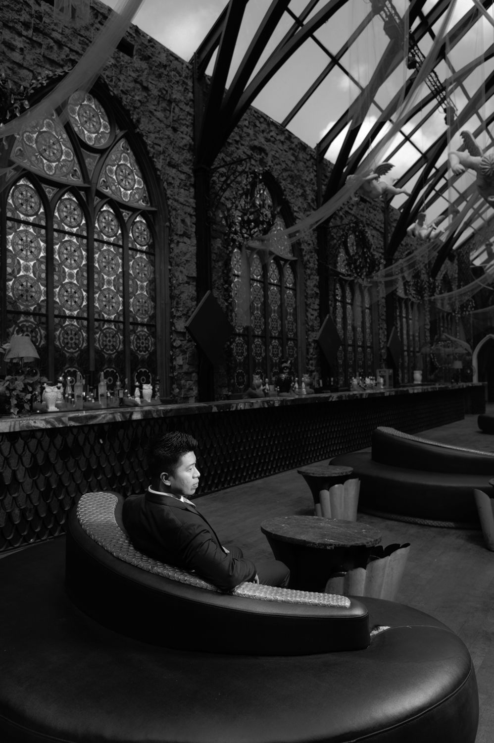 Person relaxing in a luxurious gothic-style lounge with ornate windows, captured in black and white photography.
