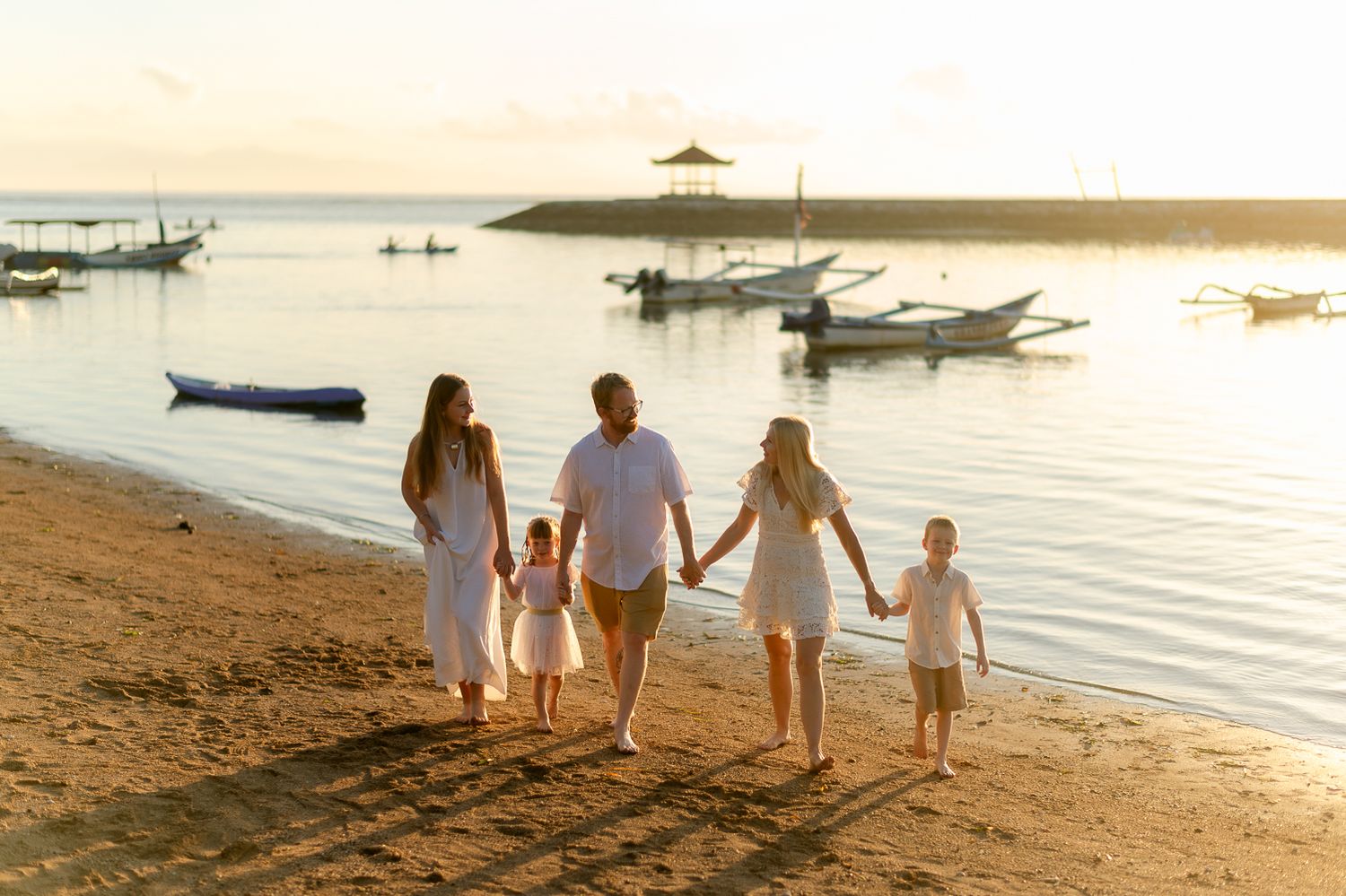 Happy family strolling hand in hand along a tropical beach during a warm golden sunset.