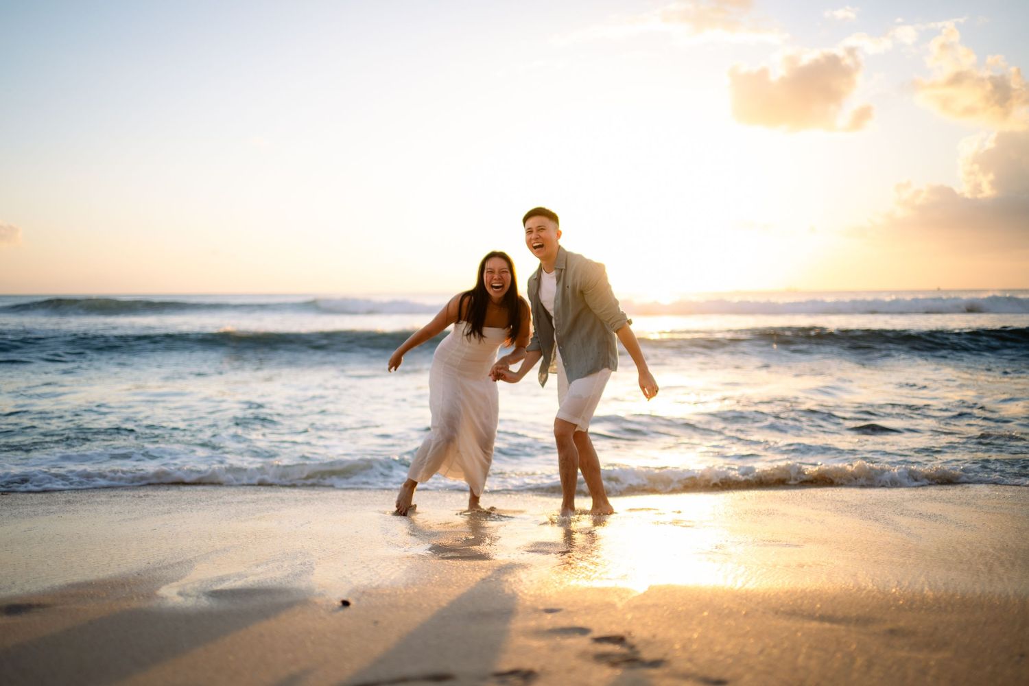 Couple running joyfully on a sandy beach at golden sunset, waves crashing behind them in a romantic seaside moment.
