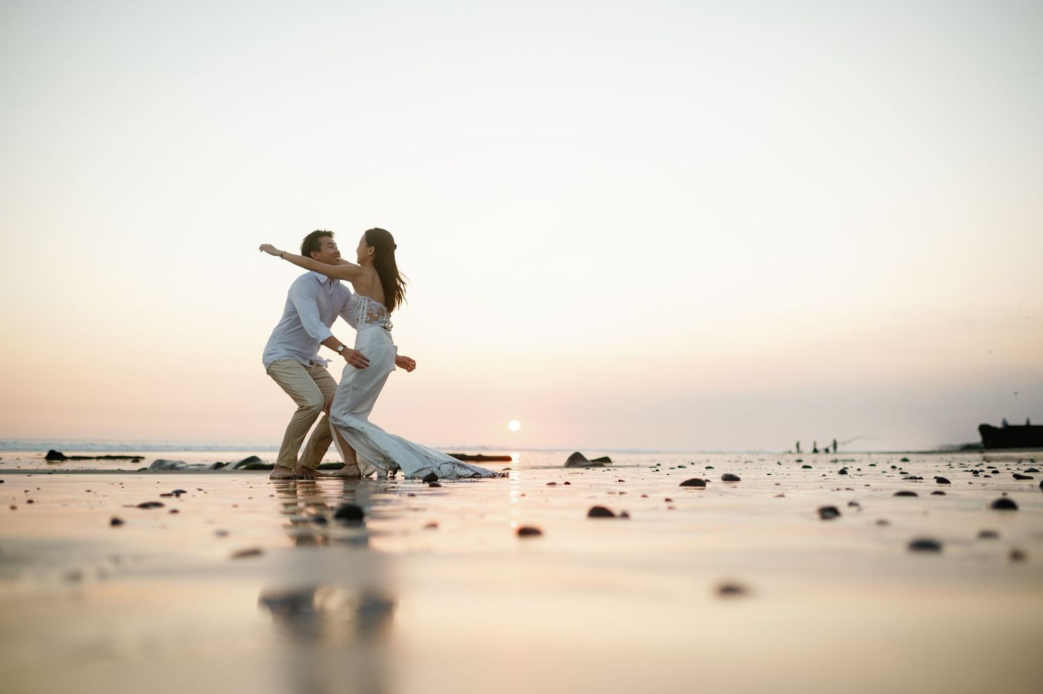 Bride and groom sharing a romantic dip kiss on a serene beach during golden hour sunset.