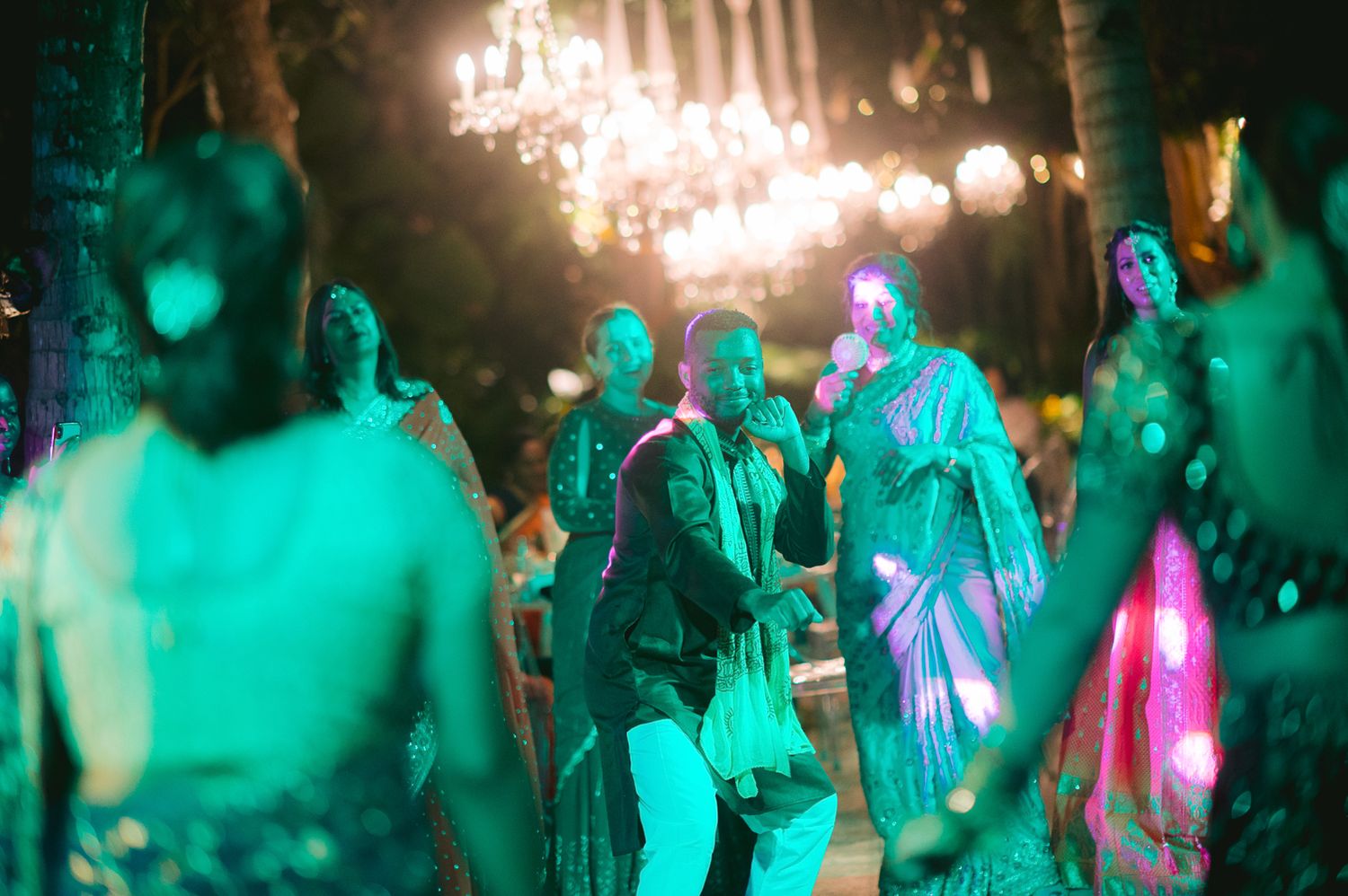 Guests dancing at an elegant outdoor evening party with green lighting and chandeliers.