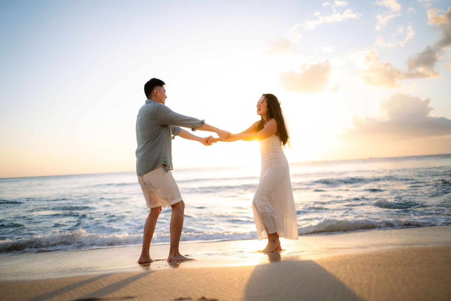 Romantic couple holding hands and dancing together on a sandy beach at golden sunset.