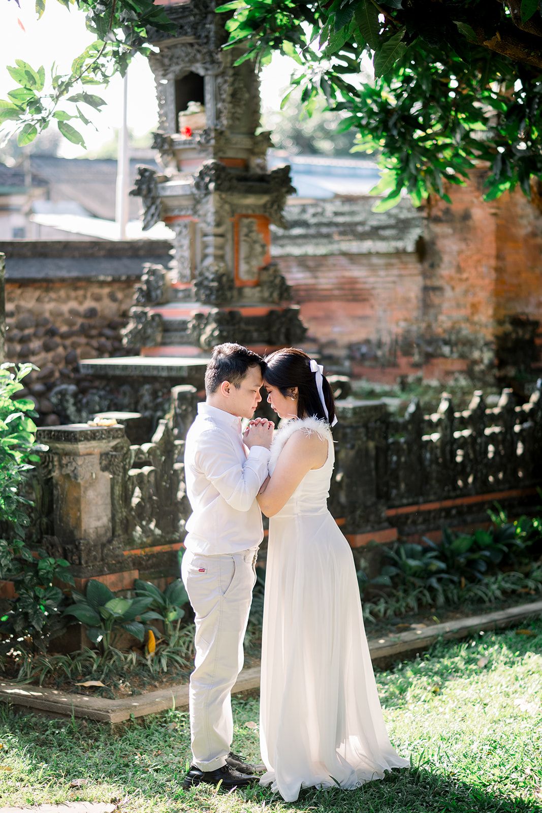 Couple in wedding attire sharing a romantic moment at a Balinese temple surrounded by lush greenery.