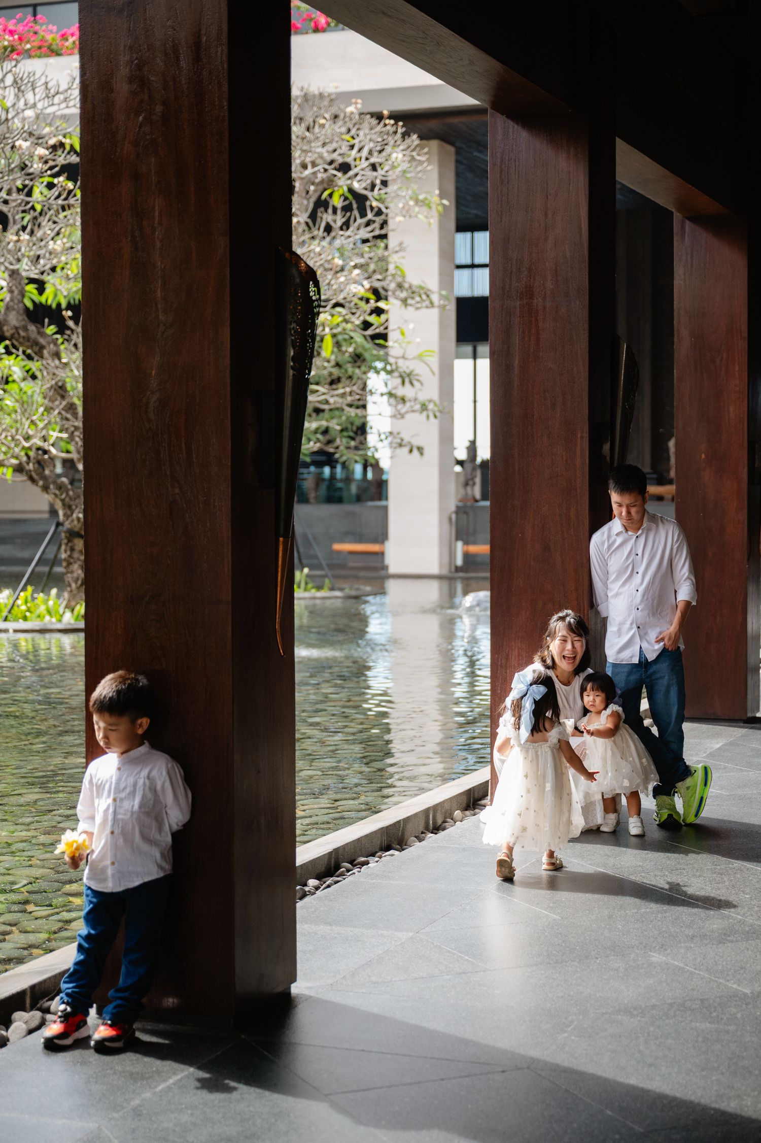 Asian family with two young children walking through an elegant open-air pavilion with reflective pool.