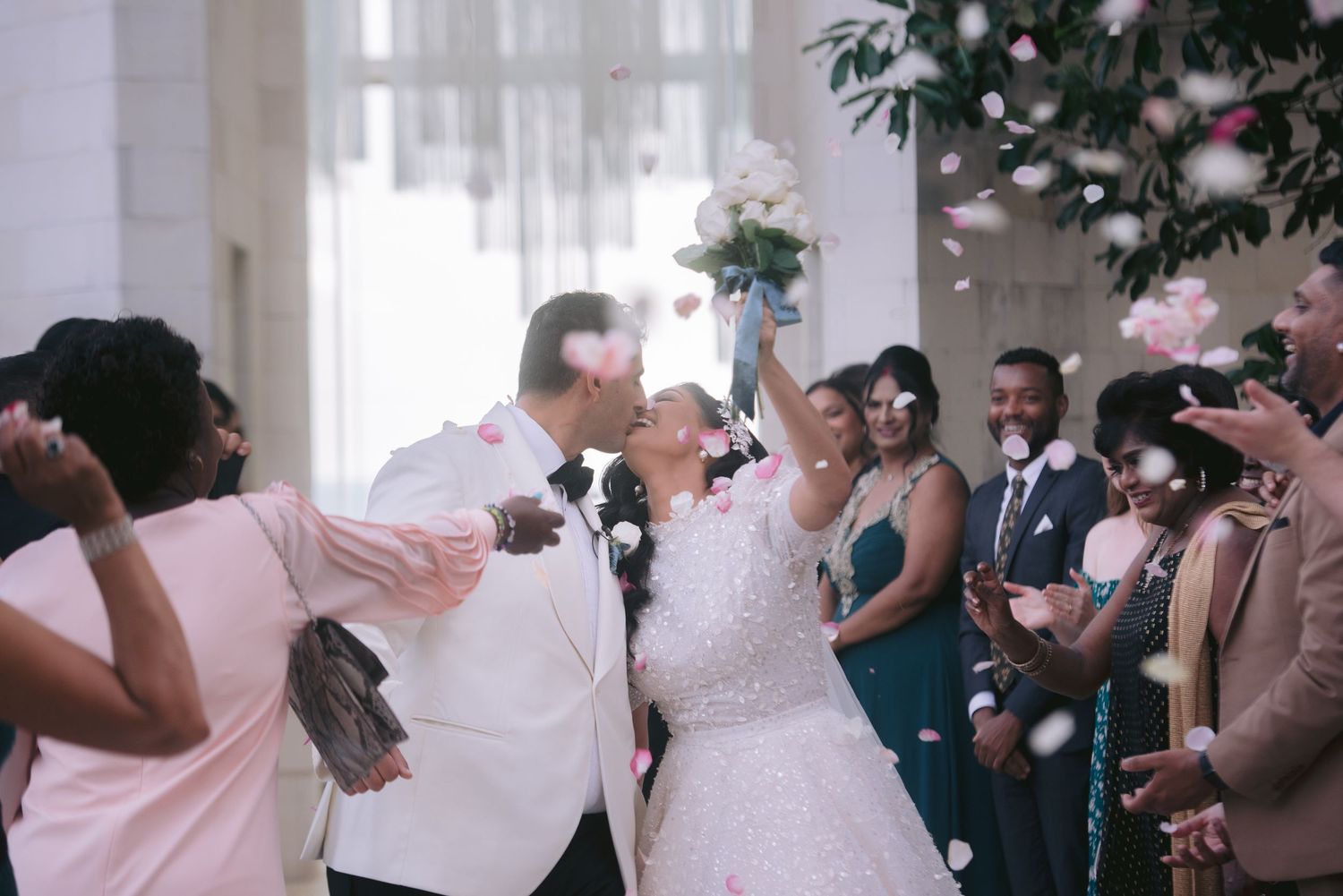 Joyful newlyweds share a kiss as colorful confetti fills the air during their elegant wedding ceremony exit.