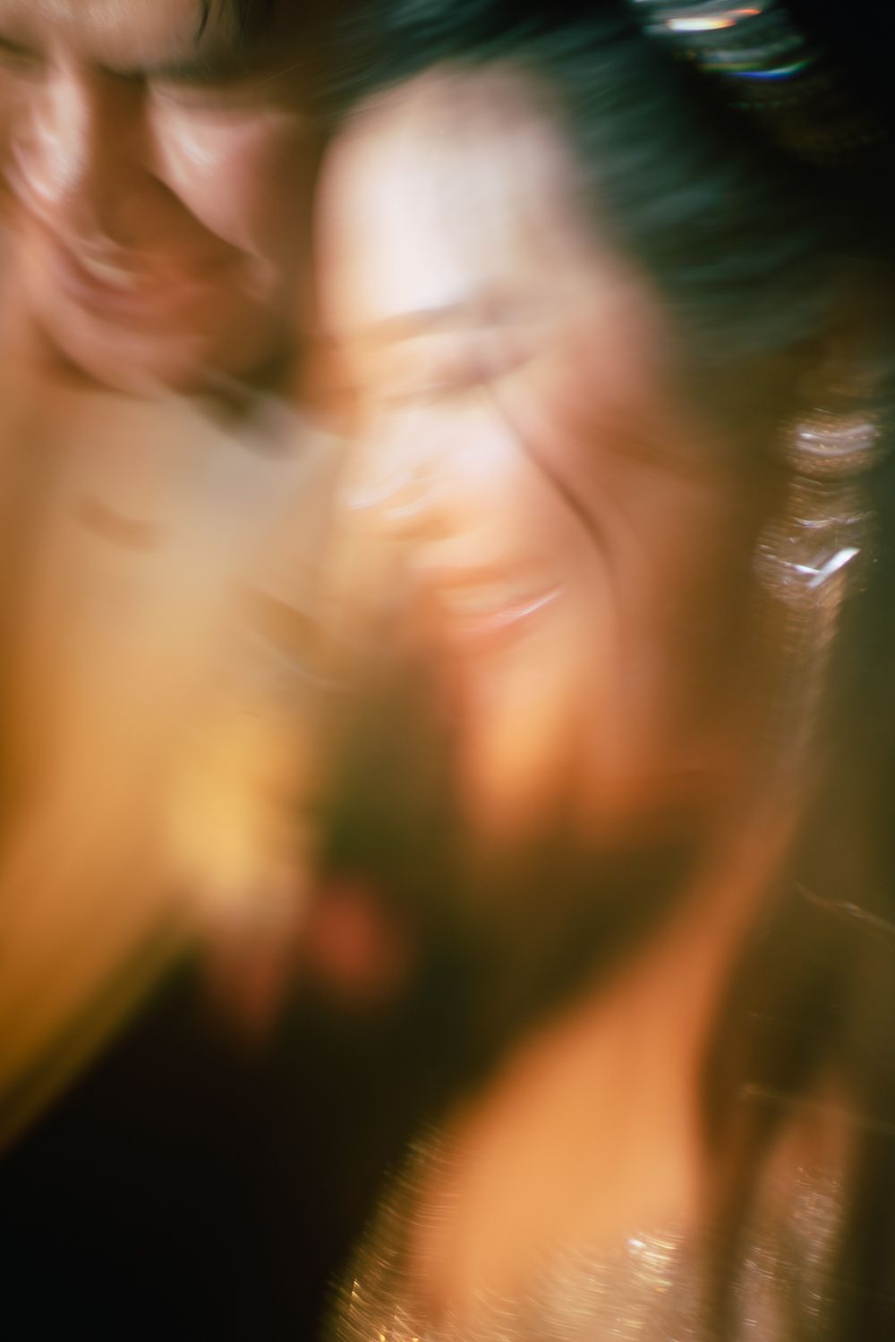 Blurry motion-blur photo of two people smiling closely together, bathed in warm golden light.