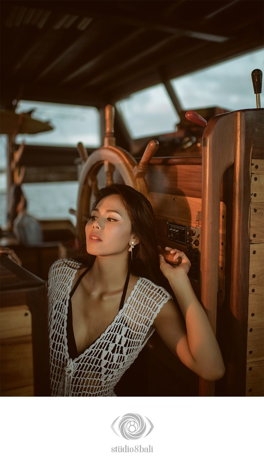 Woman in crochet top poses on a vintage wooden sailboat deck at golden hour.