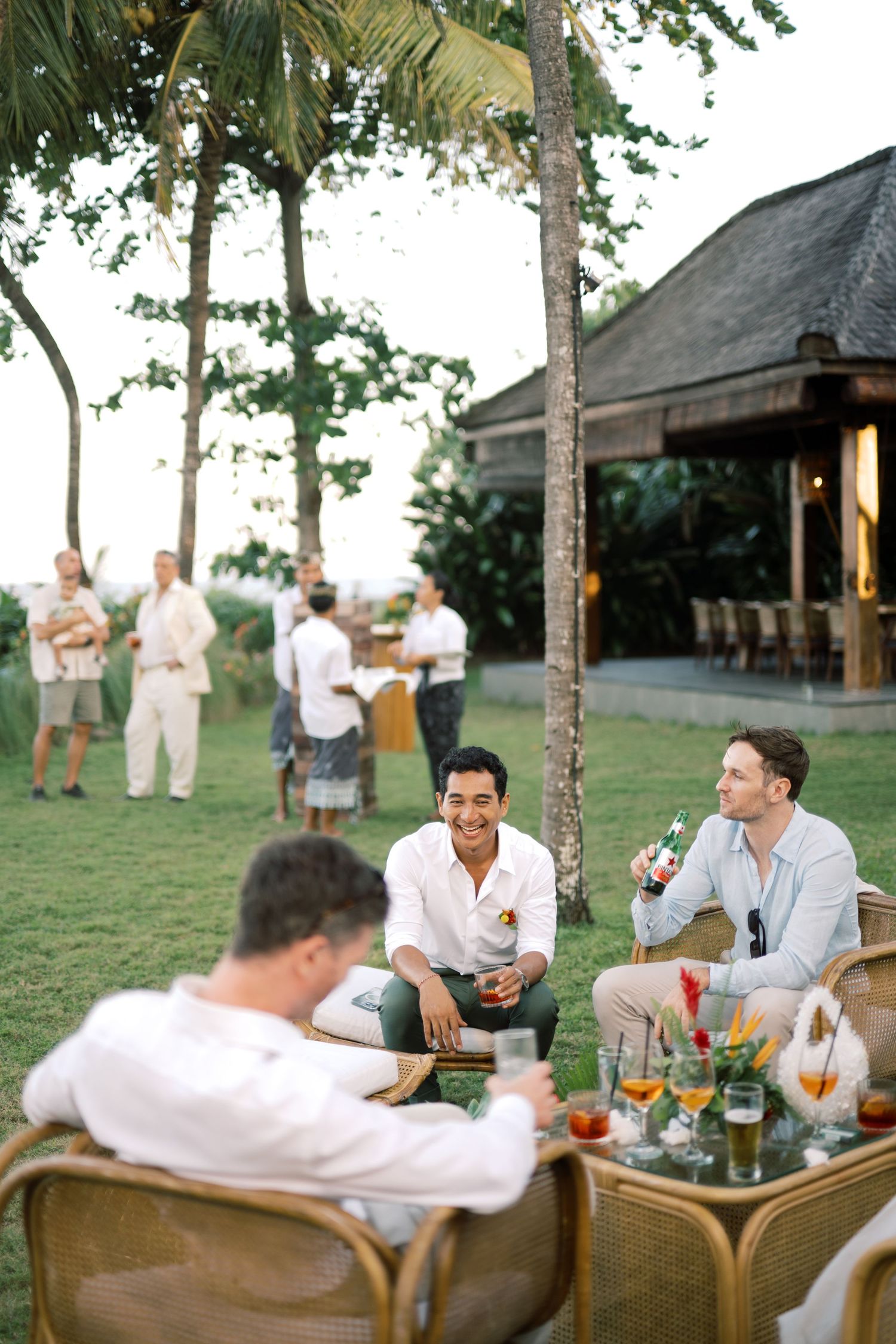 Wedding guests socializing outdoors at tropical resort reception with drinks and string lights.