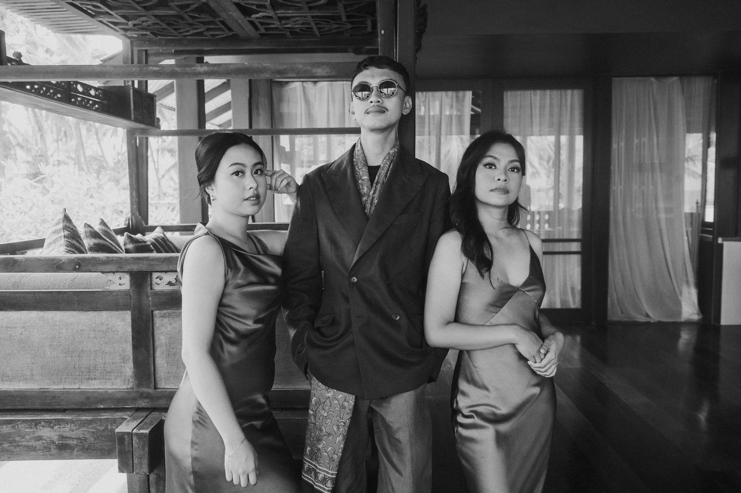 Black and white photo of three elegantly dressed people posing together in a wooden interior setting.