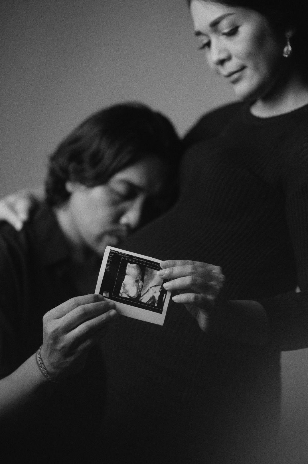 Couple in black and white photo holding an ultrasound image, sharing a tender moment anticipating their new baby.