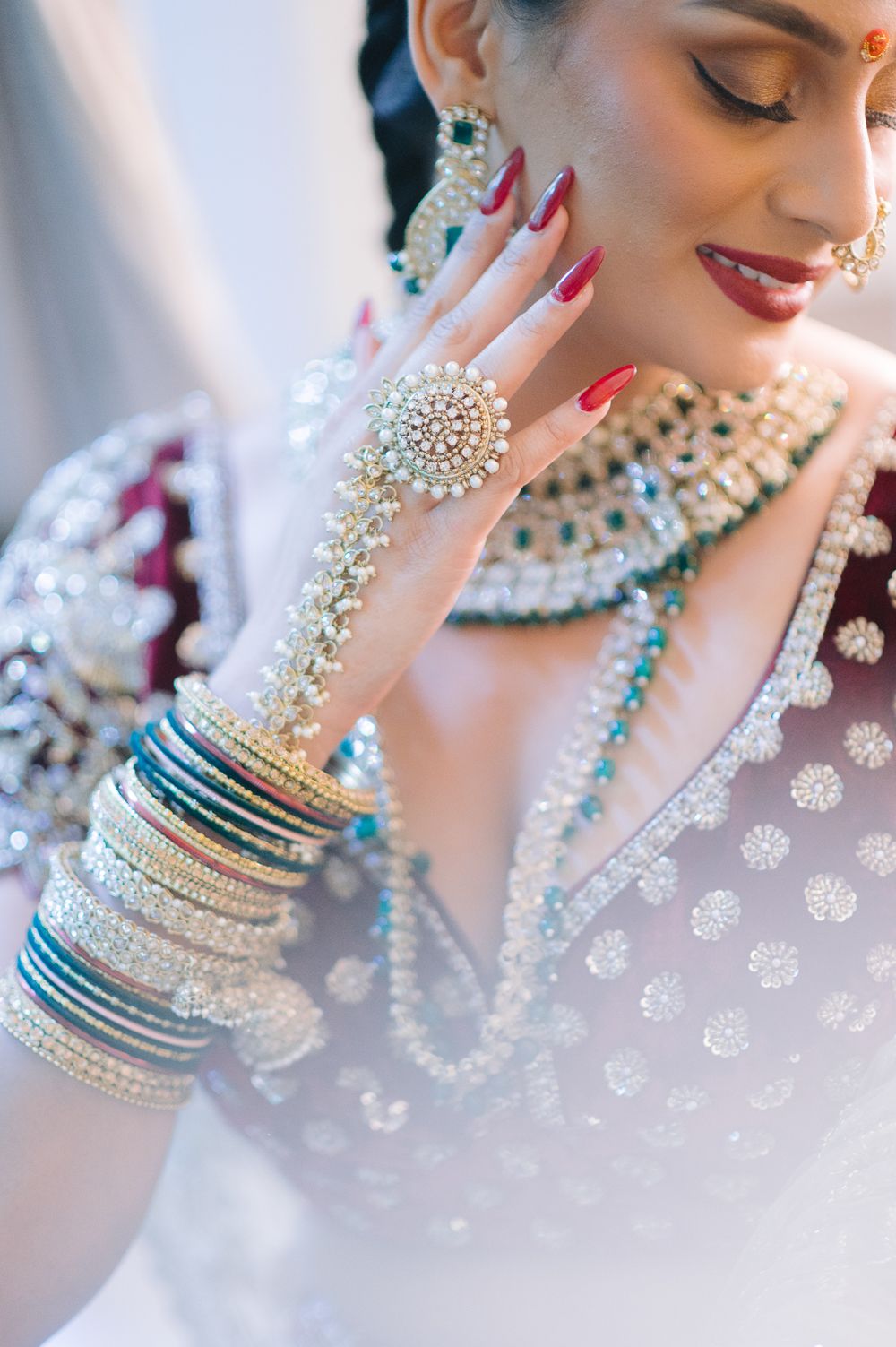 Indian bride showcasing stunning kundan jewelry, bangles, and hath phool against a white veil backdrop.