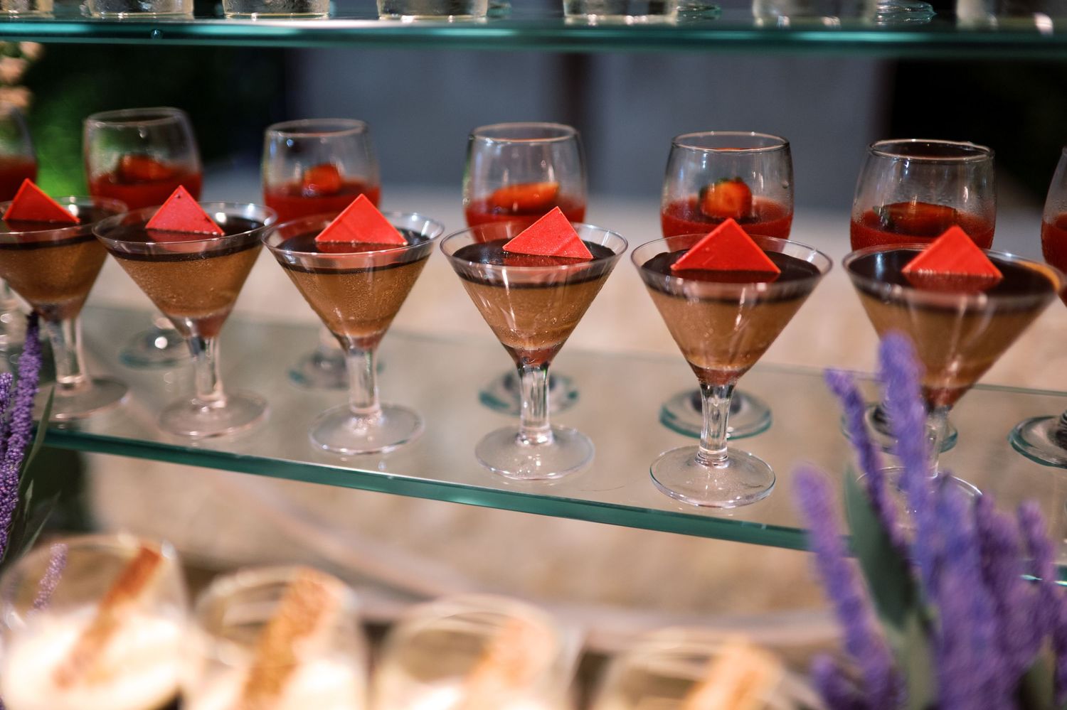 Elegant chocolate mousse desserts in stemmed glasses topped with fresh strawberries displayed on a glass shelf.
