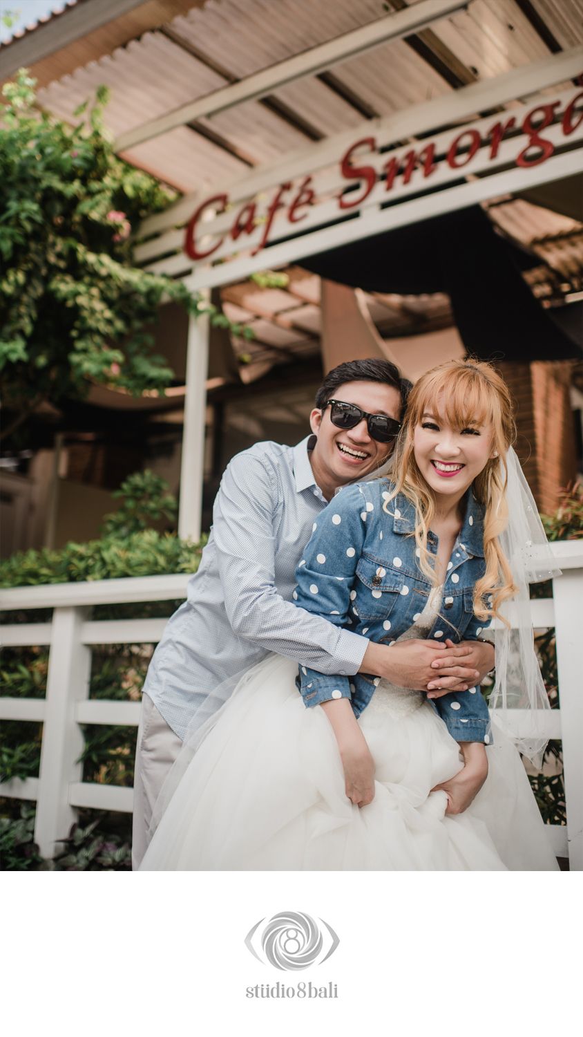 Happy couple posing in front of Cafe Smorgas, woman in polka dot top with white skirt, man in sunglasses hugging her.