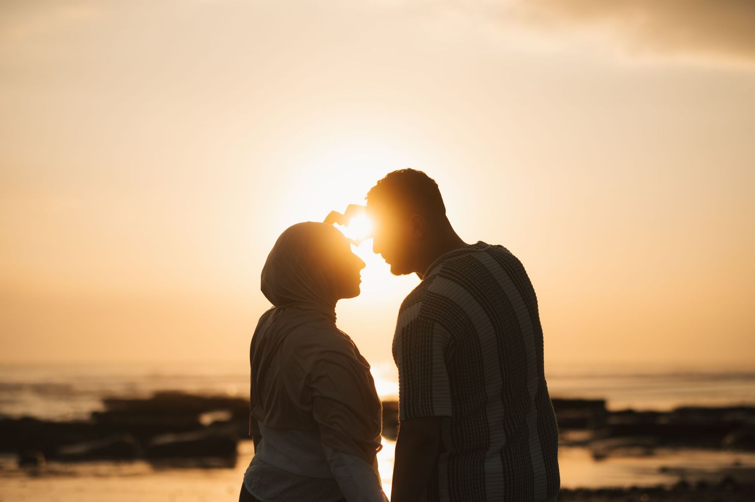 Silhouette of a romantic couple almost kissing at sunset on a beach with golden sky.