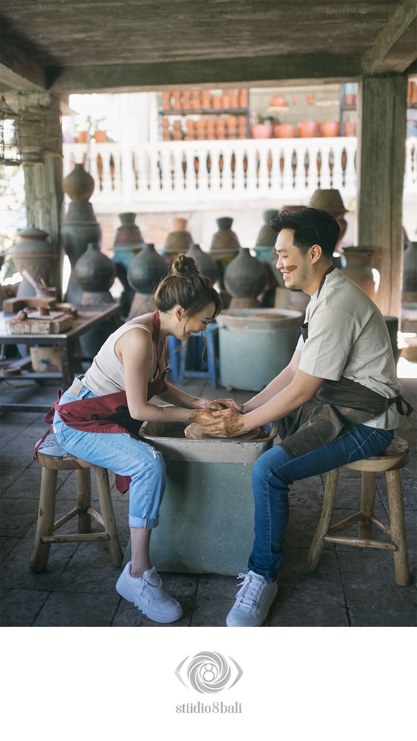 Couple sharing a romantic pottery wheel experience in a rustic ceramic studio surrounded by clay pots.