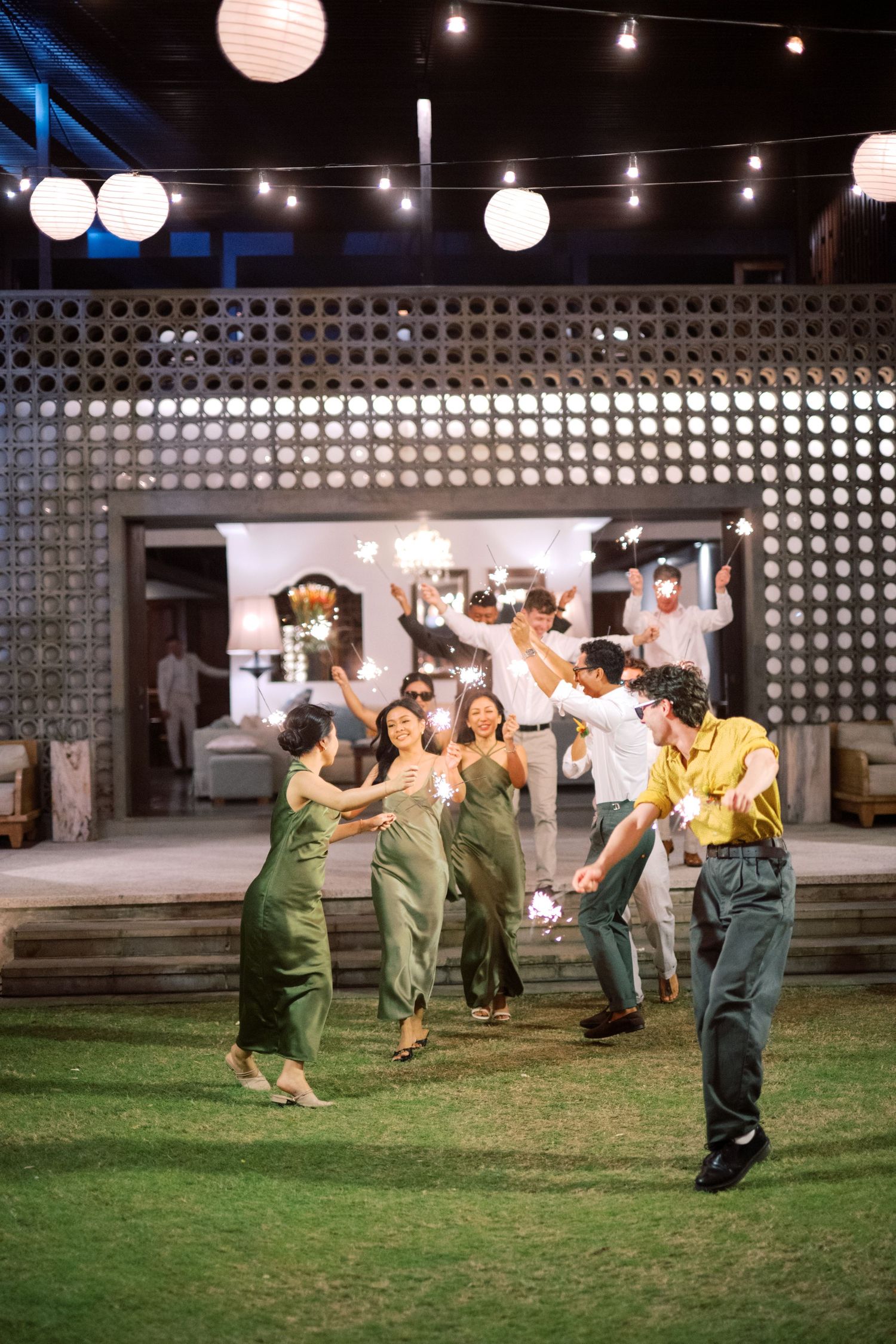 Wedding guests dance joyfully under string lights and white paper lanterns at outdoor night reception.