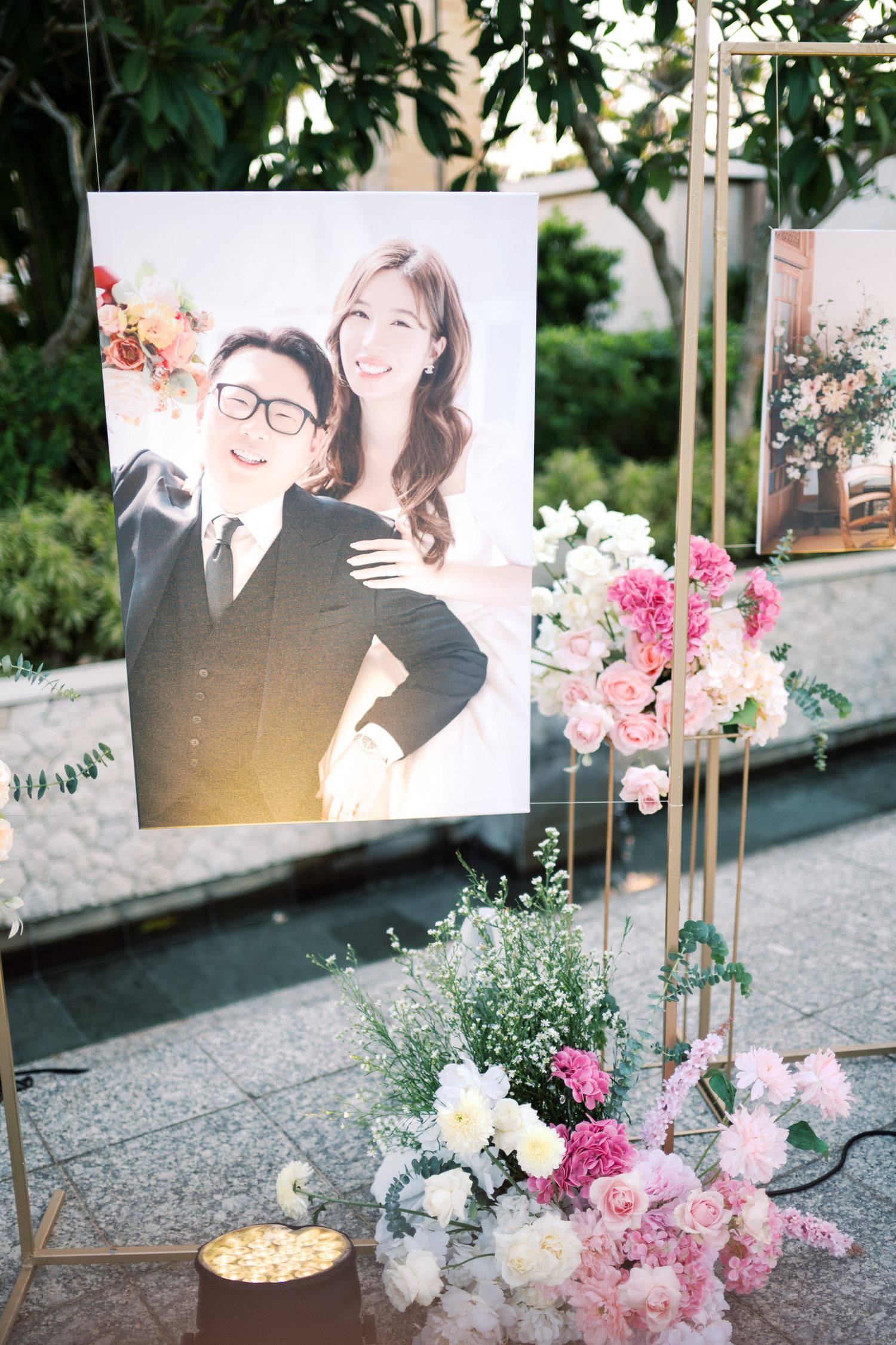 Wedding display with couple photo portrait surrounded by pink and white floral arrangements on gold stand.