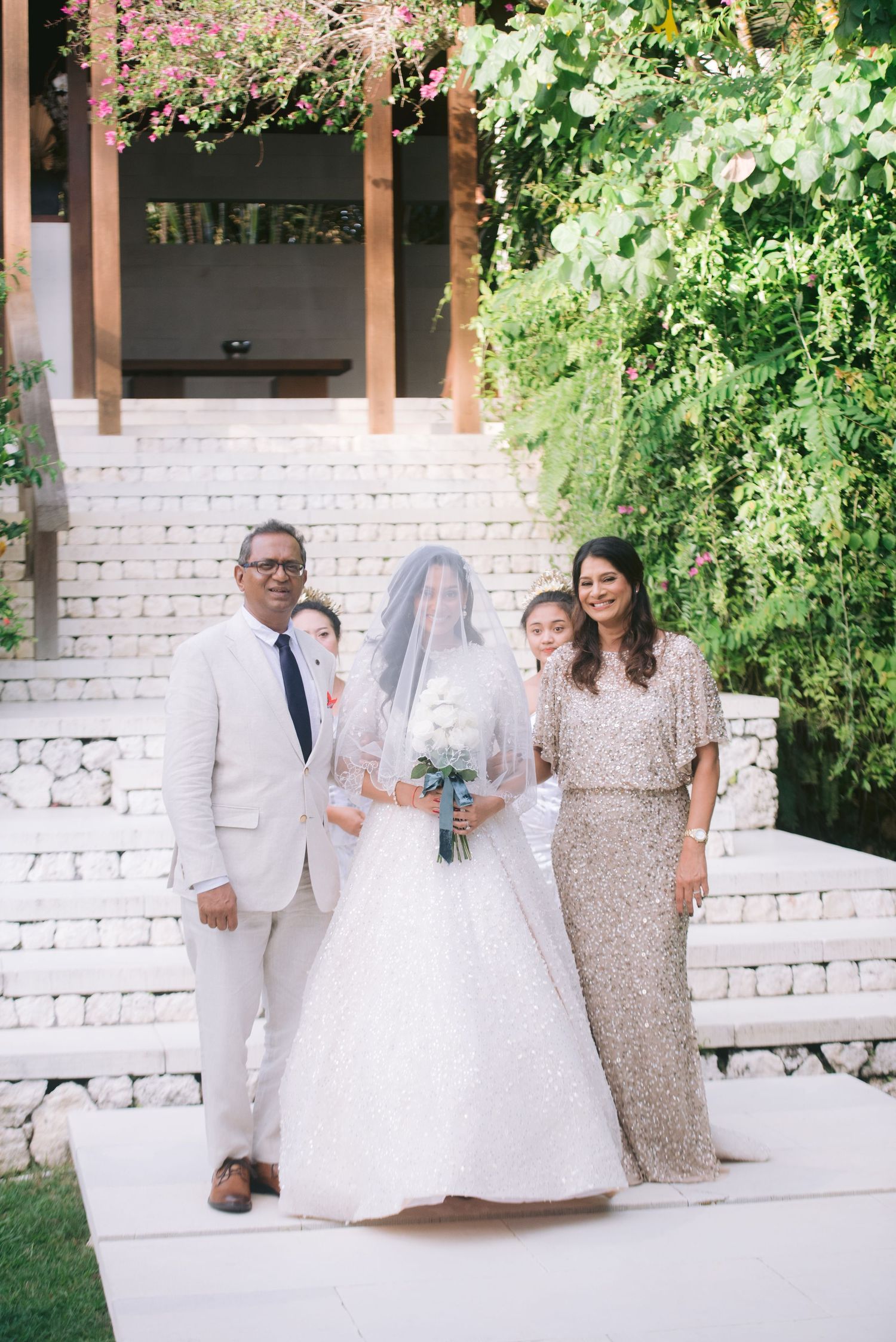 Bride in white gown and veil poses with family on outdoor steps at a garden wedding venue.