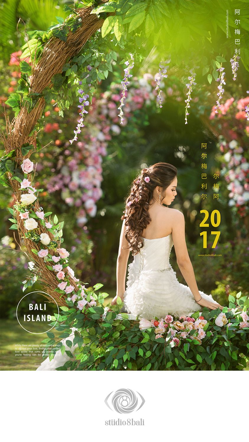 Bride in white strapless gown sits gracefully amid lush floral arch with roses and greenery in a romantic garden setting.