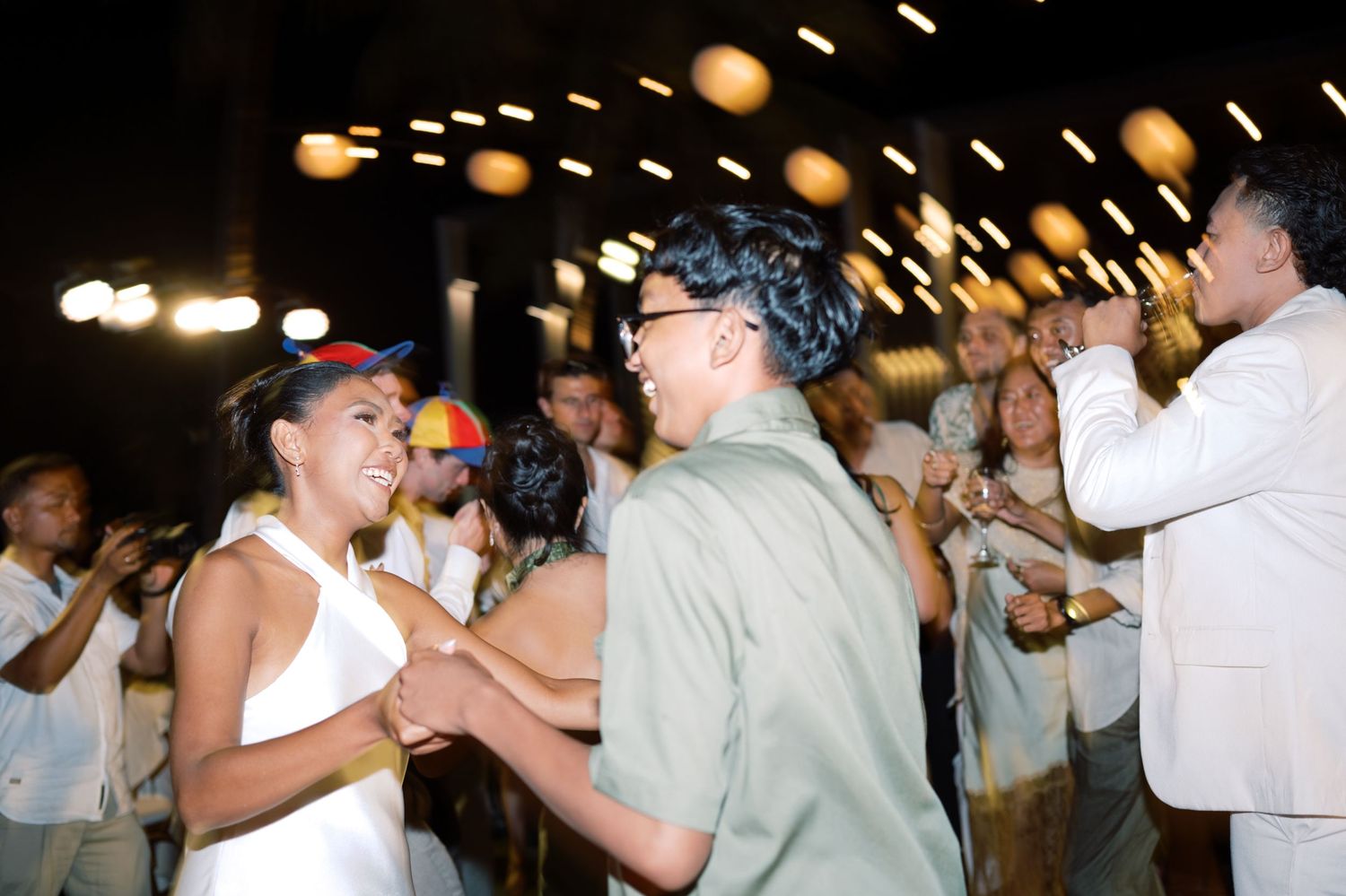 Guests dance and celebrate with bride at lively outdoor tropical wedding reception at night.