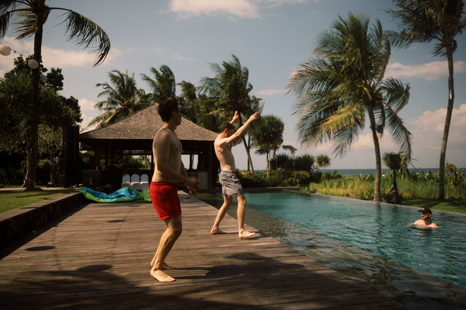 Two men playing by a tropical infinity pool with palm trees and ocean view at a luxury resort.
